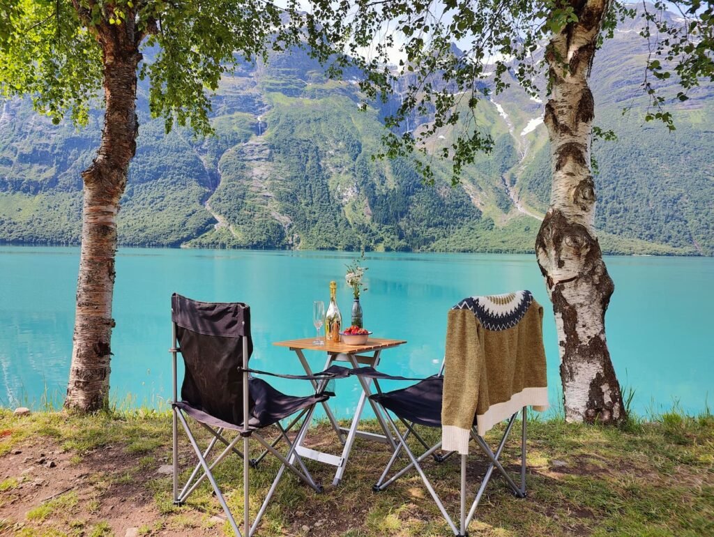 Camping by a turquoise Norwegian fjord with outdoor seating and mountain views.